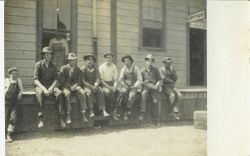 Seven men and one boy employees sitting near the office of a Graton packing house (cannery), 1912