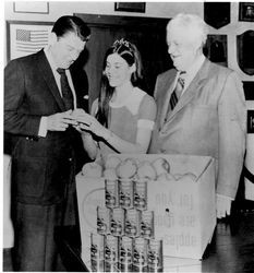 California Governor Ronald Reagan in the governor's office in Sacramento 1968 being presented with cases of apples, apple juice and apple sauce from "Sebastopol's Finest" by Sebastopol's Apple Queen with State Senator Randolph Collier looking on