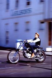 Unidentified man on a motorcycle crosses the intersection of McKinley Street and North Main Street, Sebastopol, California, 1970s