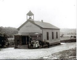 Students and their teacher at Spring Hill School stand on the school steps and two children are on horse back, 1900