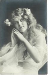 Woman in Victorian fashion with hands to her face and wearing headband with flowers and wrapped in net wrap