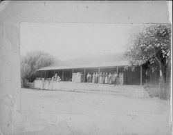 Men and women workers line the dock area of the Huntley apple dryer in Sebastopol, California, with boxes of apples behind them, 1900