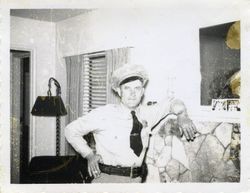 Sebastopol Police Officer Lemuel "Shorty" Plumley in uniform standing inside a house by a fireplace