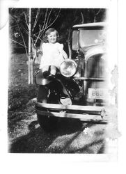 Young girl, two or three years old, sitting on fender of car with California license tag, about 1930