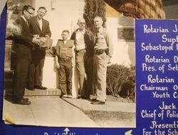 Poster photo of Delbert Triggs, president of Sebastopol Rotary, Rotarian Jack Hanley, Superintendent of Sebastopol Elementary School, Rotarian Dick Hogan, Chairman of Rotary Youth Committee and Jack Pilgrim, Chief of Police, Sebastopol and young David Collinsorth being presented with garments for the schools Safety Patrol, about 1950