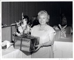 Elizabeth "Lea" Morelli Perry holding a gift box with tables and podium in background