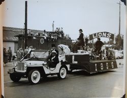 Henry Martin driving the Sebastopol Lions Club float on South Main Street past the P&SR freight warehouse in the Apple Blossom Parade, about 1956, with Edna Martin in the front seat and Edgar Herring and Billie Herring in back (Sebastopol Lions Club scrapbook photo)