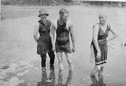 Two women and a man in bathing suits stand in the water at the beach at Bodega Bay, about 1919