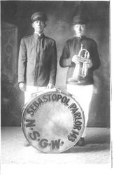 Two Native Sons of the Golden West (NSGW) band, Sebastopol Parlor 143 members Henry and Leonard Owens stand in uniforms and caps, Henry with drum and Leonard with trumpet