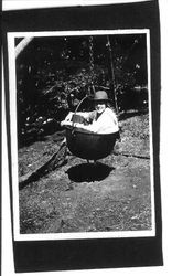 Unidentified girl sitting in a an iron rendering vat hanging from a chain, about 1920