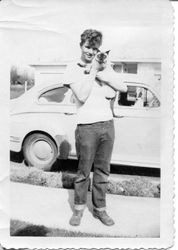 Unidentified teenage boy holding a cat in front of a 1947 or 1948 Chevrolet