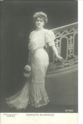 Lyric soprano and musical comedy start Christie McDonald in Victorian fashion with flowers in her hand and standing against staircase railing