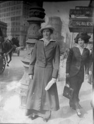 Unidentified woman, about 1915, in suit and hat standing on the sidewalk of an unidentified a big city