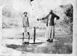 Woman and a girl stand by a water pump, about 1915