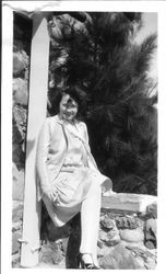 Bunni Cornelia E. Myers seated on a stone wall with pine trees in the background