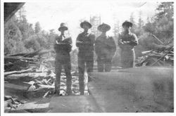 Four men stand among cut lumber