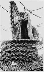 1914 Gravenstein Apple Show display or a round apple covered pedestal with harp made of apples being played by King Gravenstein mannequin dressed in cape made of apple slices