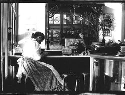 Interior photo a of soda fountain with woman seated at the counter and another woman beind the counter in Worth's Drugstore in 1903