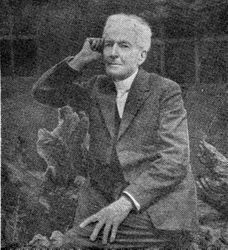 Luther Burbank in his later years, about 1920, seated on what appears to be the stump of an up-ended tree