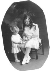 Bunni Cornelia E. Myers seated on a chair with a book and a younger child standing and looking at the book, about 1915