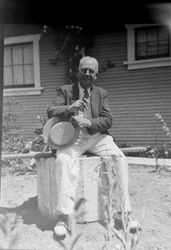 An unidentified man sits in a yard next to a house