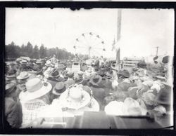 Large crowd with their backs to the camera listening to two men who appear to be speaking to the crowd