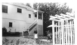 Bunni Streckfus standing outside in a garden area behind a two-story wooden clapboard house in 1945