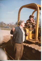 Don Hallberg standing next to the grader as ground is being prepared for construction of the Hallberg Apple Farm fruit stand and bakery, about 1982