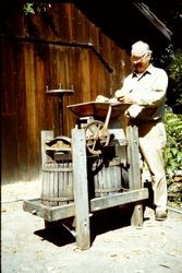 Man standing at a hand-cranked apple press (juicer), about 1980