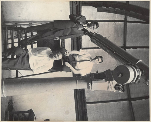 3 men posed at the base of a telescope