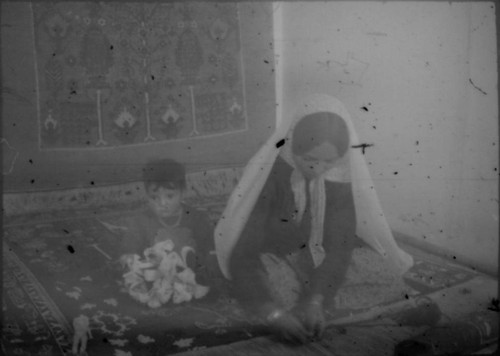 Unidentified woman and child in traditional clothing seated on a carpet