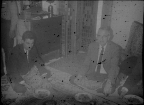 Two unidentified men eating a meal on a carpet