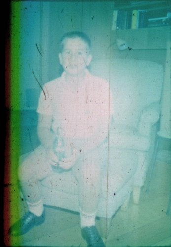 Unidentified young boy seated on an ottoman, drinking a Coke
