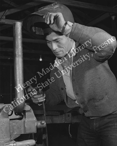 Former California mechanic Chester Ishii repairing piece of farm machinery at Rohwer Relocation Center