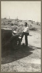 [Man standing next to car with foot on tire]