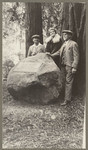 [Two men and one woman posing in front of boulder with plaque]