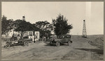 [Family in front of house with parked cars in foreground and oil well on right]