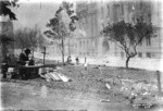 [Author Henry Lafler at typewriter next to fresh graves. Portsmouth Square. Hall of Justice in background, right]