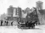 [Man in car parked near ruins. Unidentified photographer at left. Frames of Newman & Levinson and Whittell buildings (near Union Square) in background. From near Grant, O'Farrell and Market Sts.?]