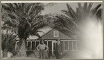 [Alfred Fuhrman and man standing near house with palm trees]