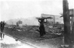 [Woman gathering roofing tin among ruins]