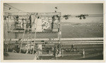 Looking directly east from the midspan crossbridge showing the mechanism for the transfer of wires during spinning operations. The spinning wheels may be seen in position to receive wires for transfer. Also, the completed cable strands are seen above the footbridge. In the distance, on the right, there is a glimpse of San Francisco. G 333