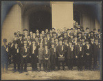 [Group portrait of men, women and boys standing on steps of building]