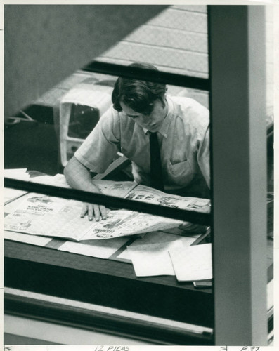 An individual reading a newspaper in Honnold Library, Claremont University Consortium