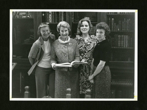 Four librarians stand side by side smiling in Denison Library, Scripps College