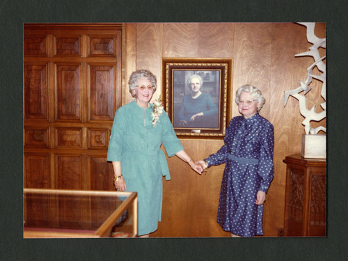 Dorothy Drake and Clara Breed stand holding hands by Dorothy's portrait, Scripps College