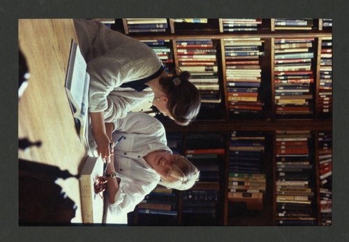 Two students discussing a book at a table in Denison Library, Scripps College
