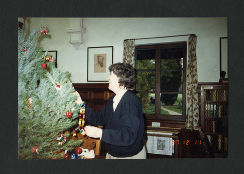 A woman puts ornaments on a Christmas tree, Scripps College