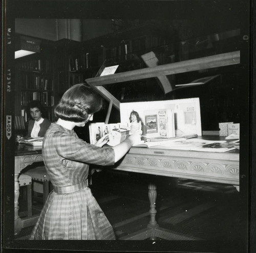 Student librarian positioning a doll in a display case in Denison Library, Scripps College