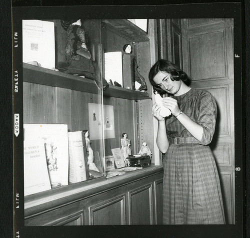 Student librarian looking at one of the dolls on display in Denison Library, Scripps College